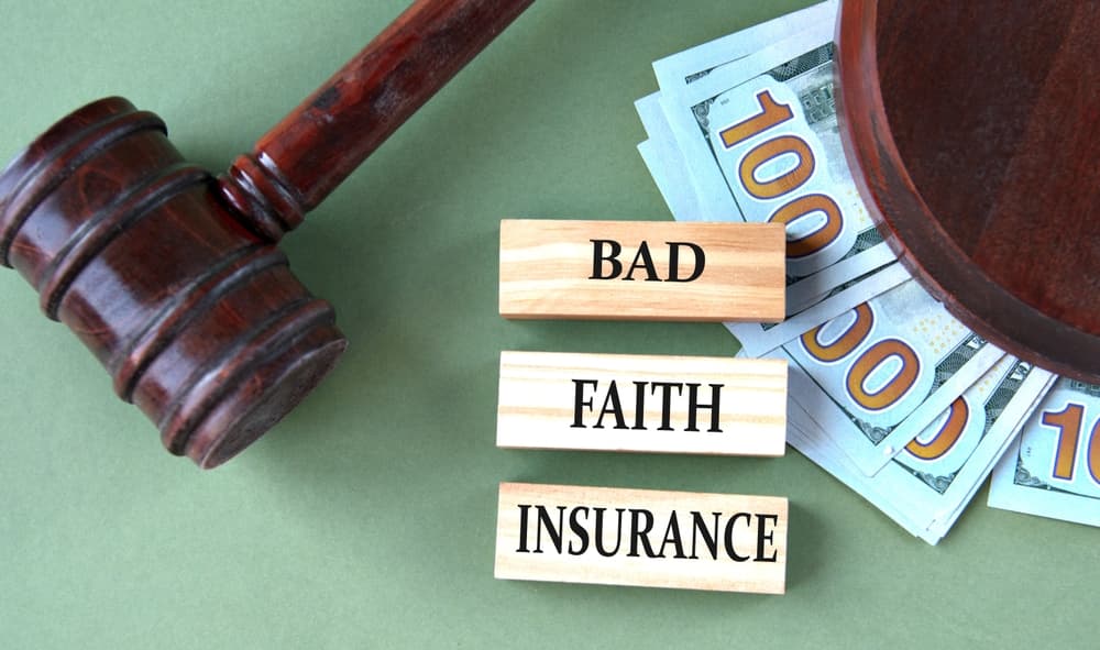 BAD FAITH INSURANCE - words on wooden blocks against the background of a judge's gavel and banknotes

