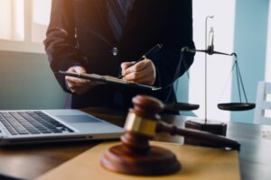 Attorney reviewing legal documents at a desk with a gavel, scales of justice, and laptop in a law office setting.