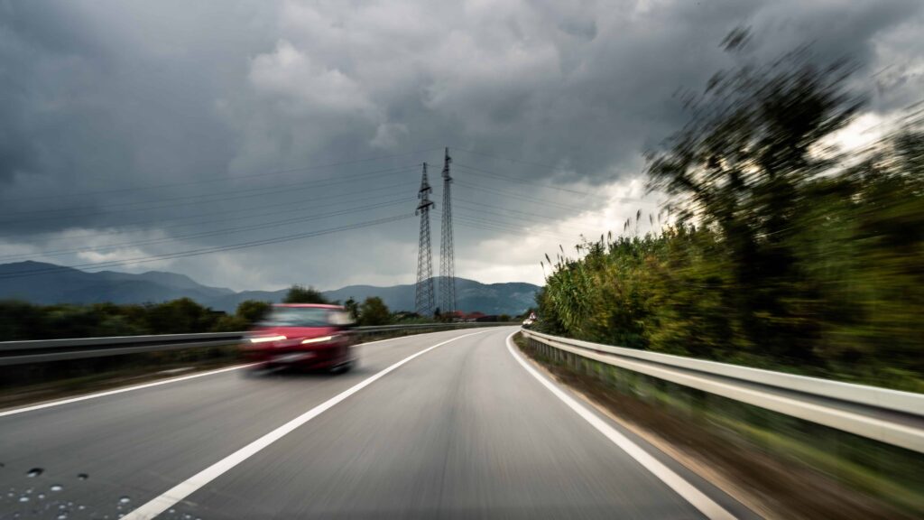 Car speeding on a wet highway under stormy weather conditions, illustrating dangerous driving risks.