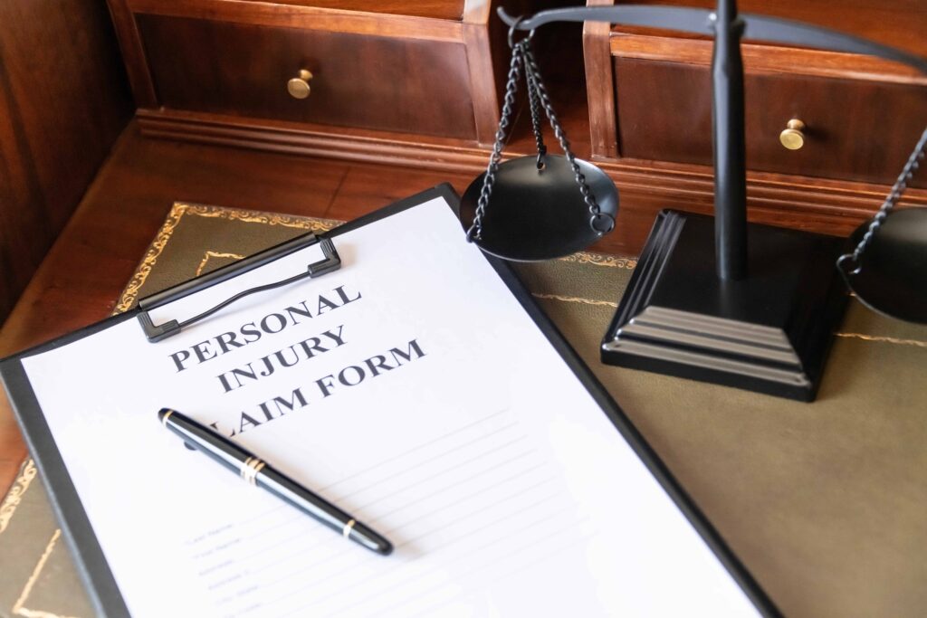 Personal injury claim form on a clipboard with pen and justice scales on a lawyer’s desk.