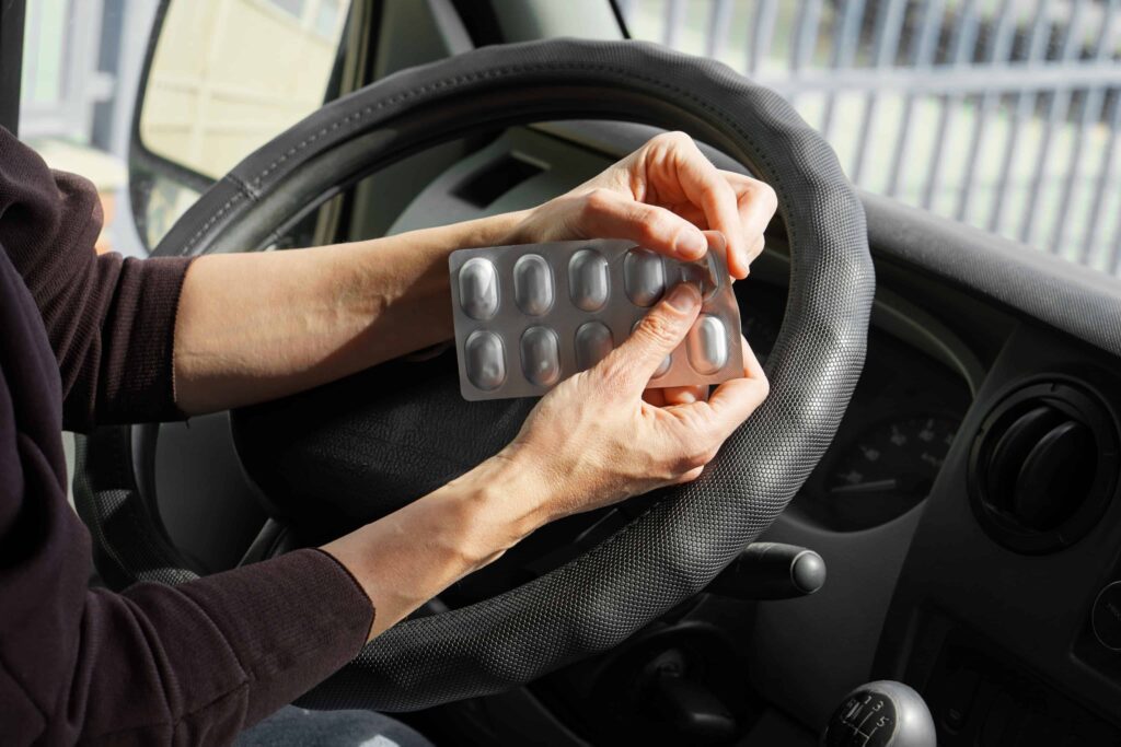 Driver opening a blister pack of medication while sitting behind the wheel.