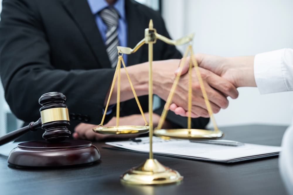 How an Attorney Helps Secure a Fair Car Accident Settlement Attorney and client shaking hands across a desk with legal documents, gavel, and justice scales symbolizing a car accident settlement agreement.