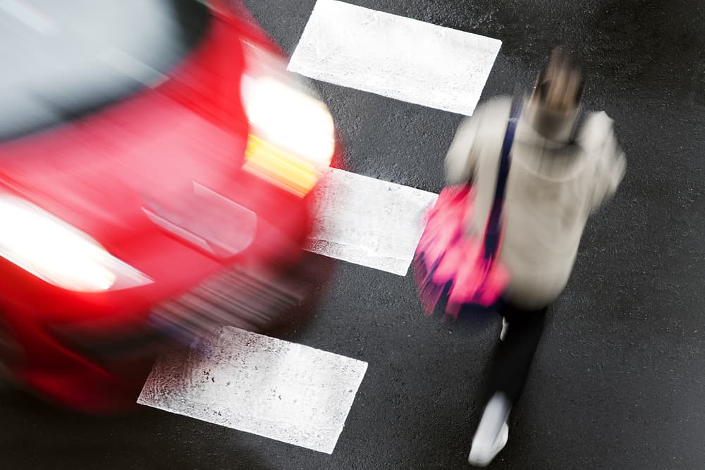 Pedestrian Accident Risk – Speeding Car Approaching Crosswalk Pedestrian crossing street as a speeding red car approaches, illustrating risk and danger in pedestrian accident situations.