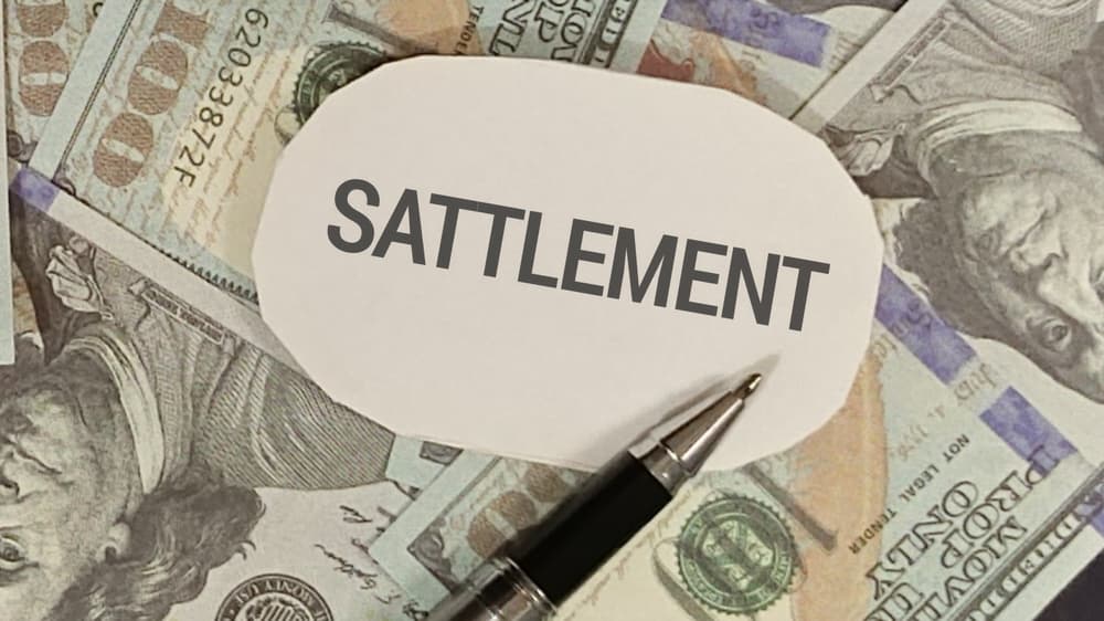 Fair Settlement for Pain and Suffering Compensation Settlement text with pen placed over spread of hundred-dollar bills representing financial compensation for pain and suffering claims.