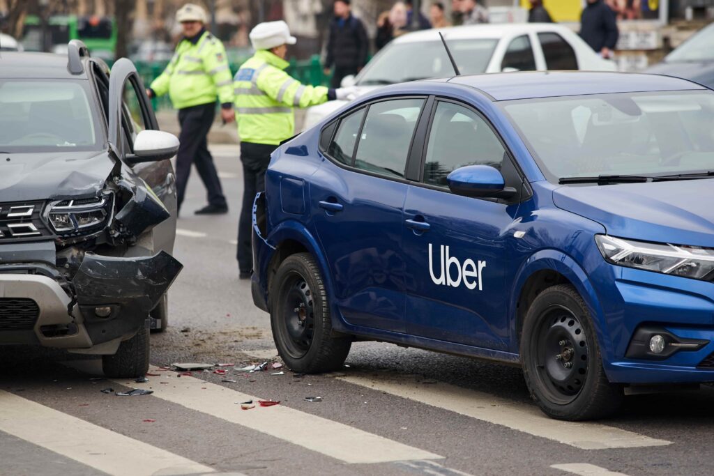 Uber vehicle involved in a traffic accident with visible car damage and police officers responding at the crash scene. Uber vehicle involved in a traffic accident with visible car damage and police officers responding at the crash scene.